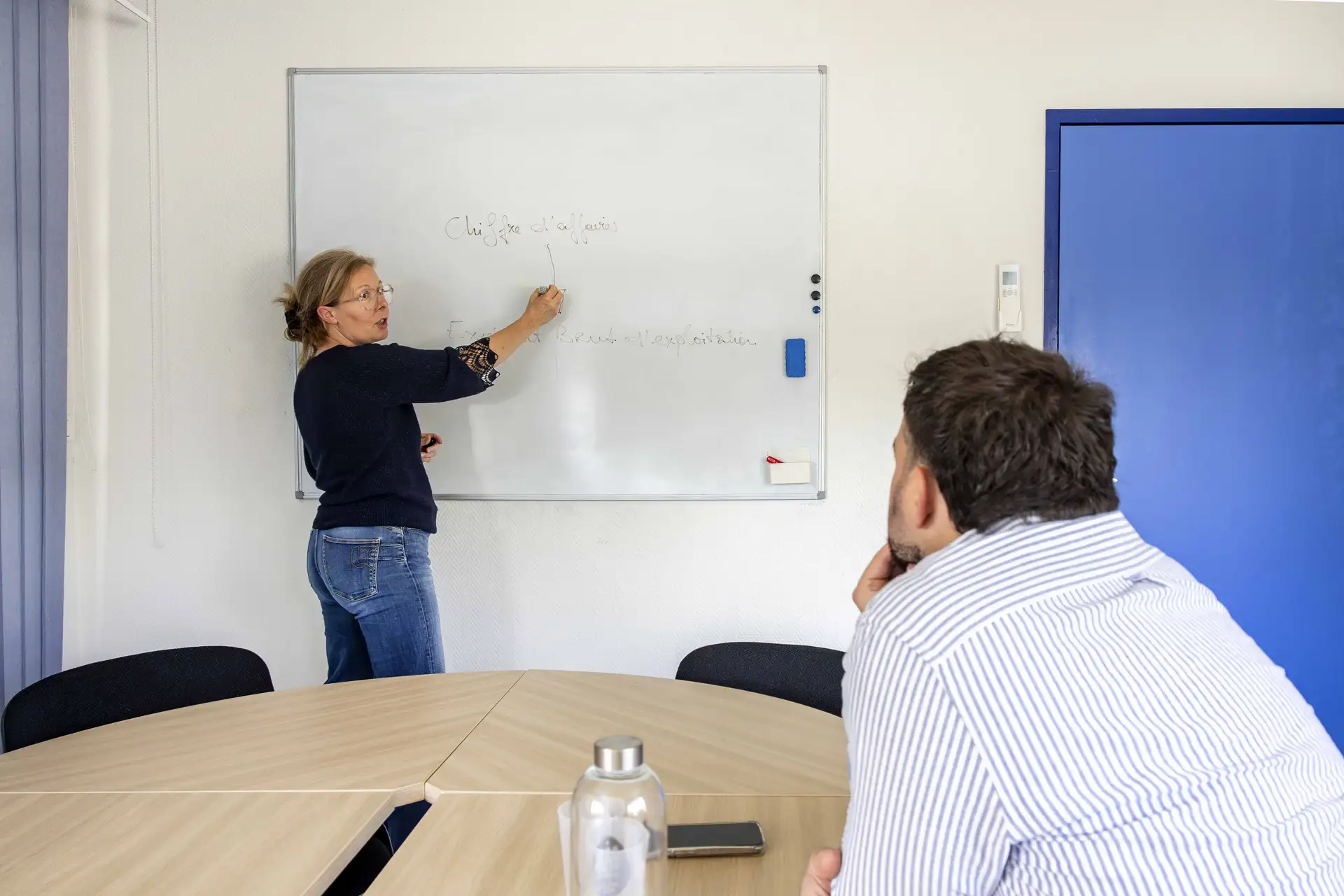 Emmanuelle Monroche anime une formation à la gestion devant un tableau blanc avec un dirigeant